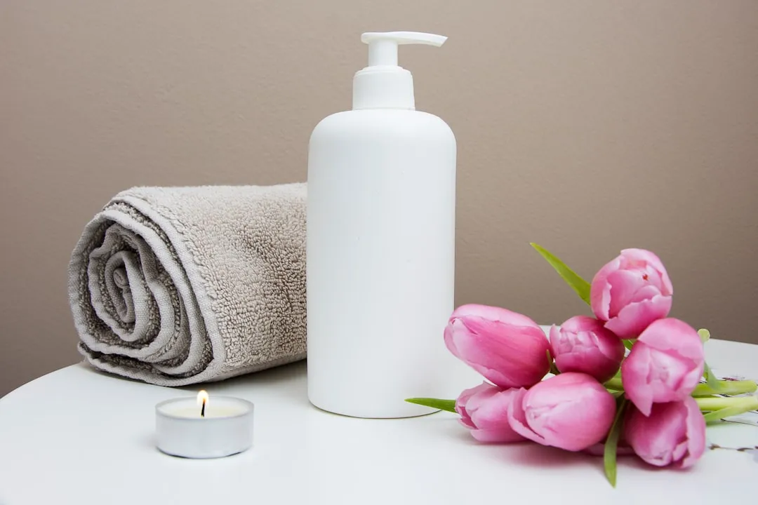 Illustrative rolled towel beside a pump bottle and pink flowers