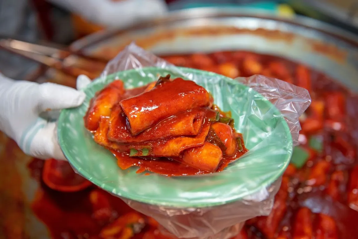 A hand holding a plate of red-sauce tteokbokki at Bupyeong Kkangtong Market in Busan