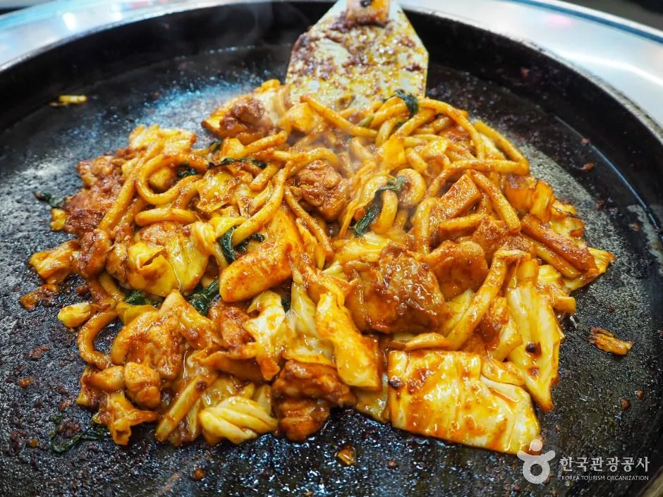 Dakgalbi with chicken cabbage and noodles cooking on a black iron griddle