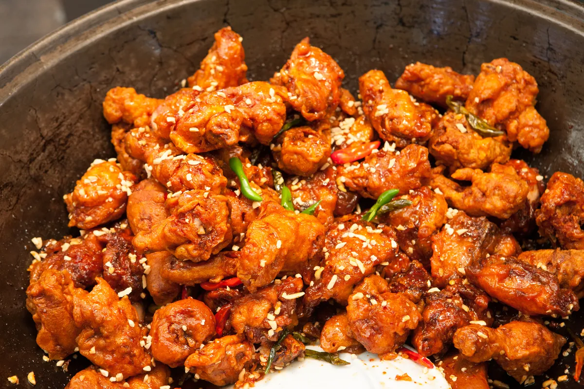 Dakgangjeong coated with red sauce in a large market cooking pan