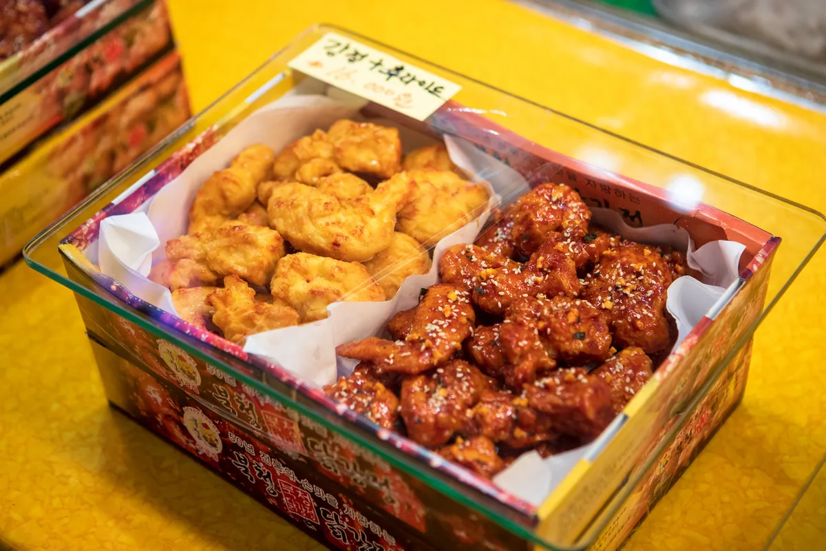 Box holding plain fried chicken beside dark sauce-coated Dakgangjeong