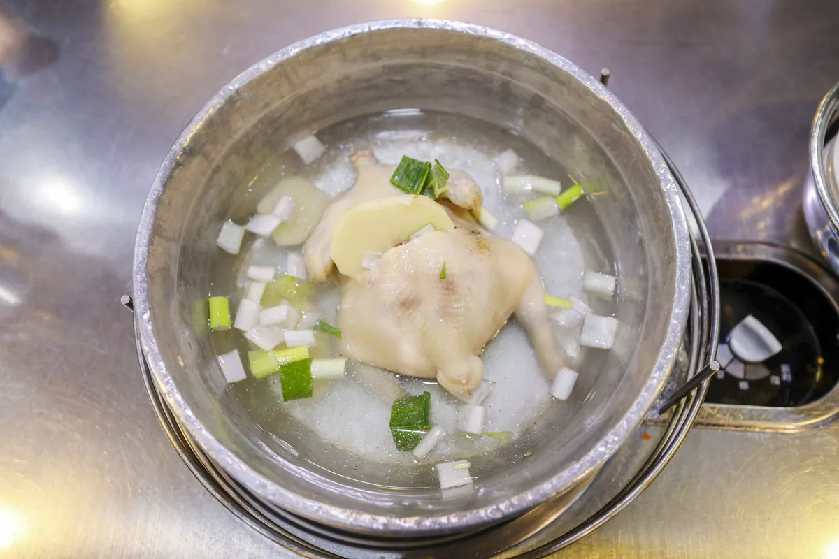 Overhead view of dakhanmari with chicken and chopped green onions in clear broth