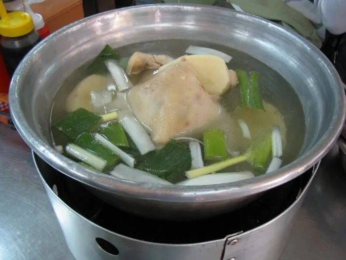 Dakhanmari in a stainless-steel pot on a tabletop burner with chicken and green onions in broth