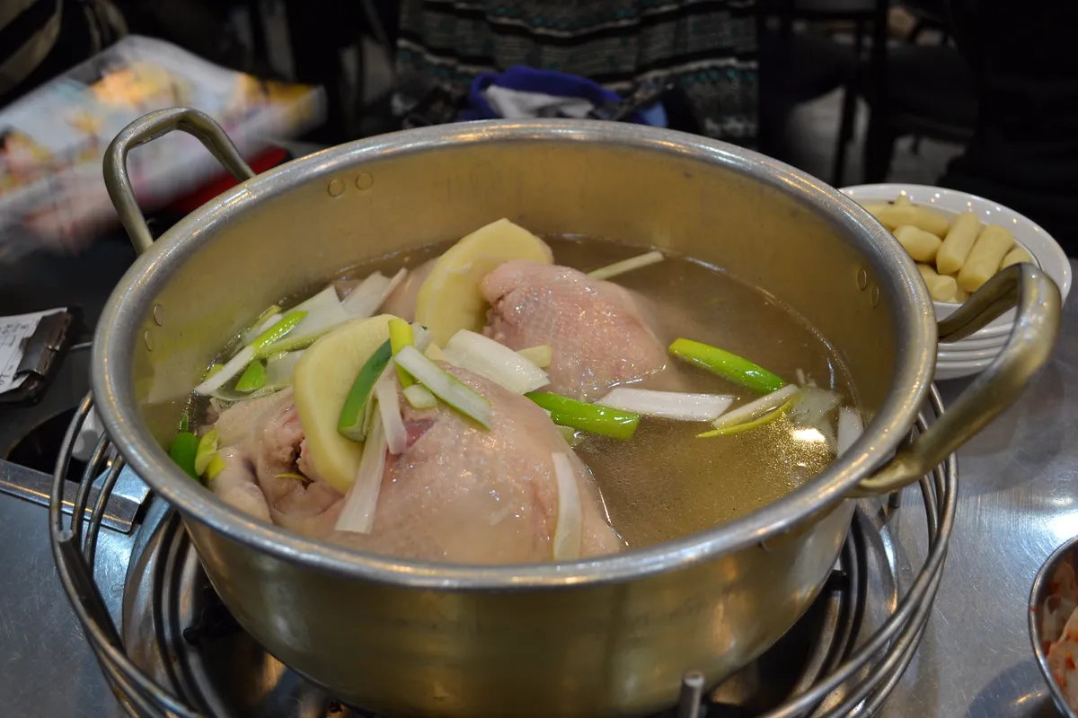 Dakhanmari in a metal pot on a tabletop burner with chicken and green onions surrounded by side dishes