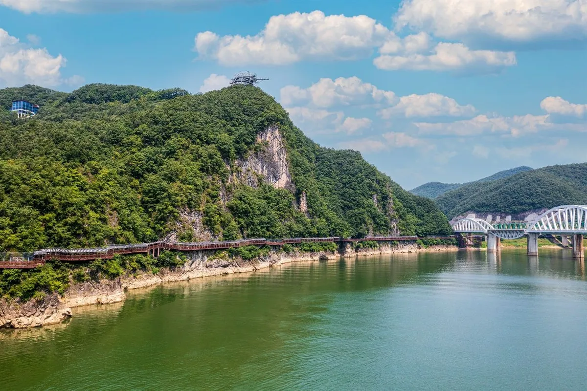 Wide view of Danyanggang Jando Trail below a wooded cliff beside the Namhangang River