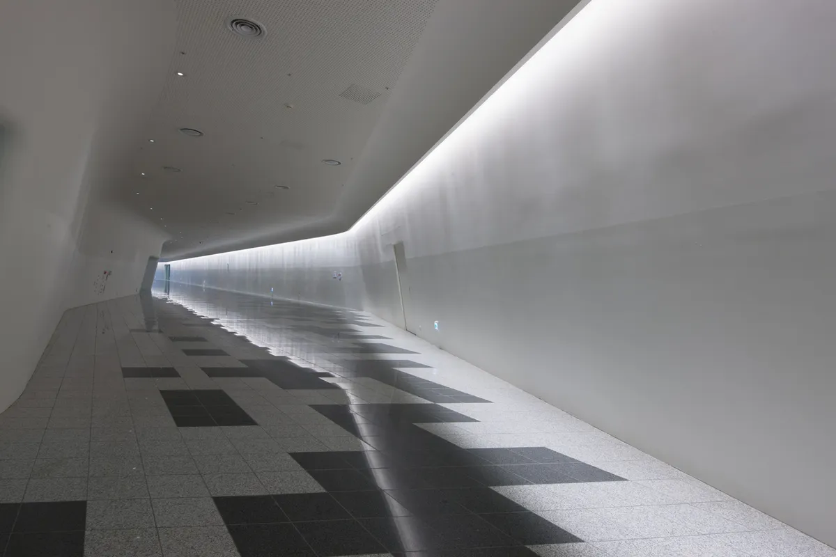 Curved interior passage with wall lighting and dark floor inlays at Dongdaemun Design Plaza