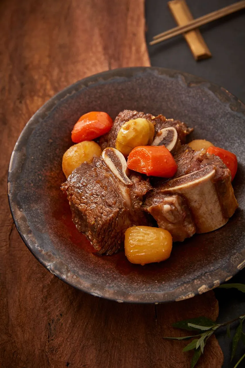 Galbijjim beef short ribs with carrots and braised vegetables on a dark plate