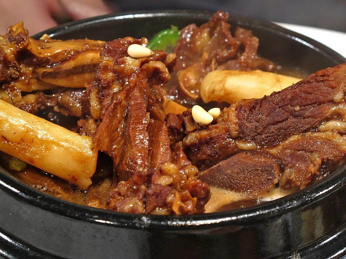 Bone-in galbijjim served in a black bowl with braised vegetables and pine nuts