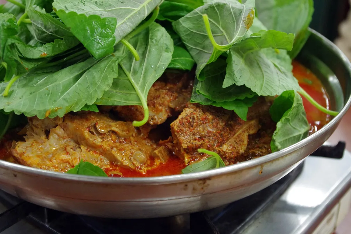Gamjatang pork backbone pieces under leafy greens in a metal cooking pan