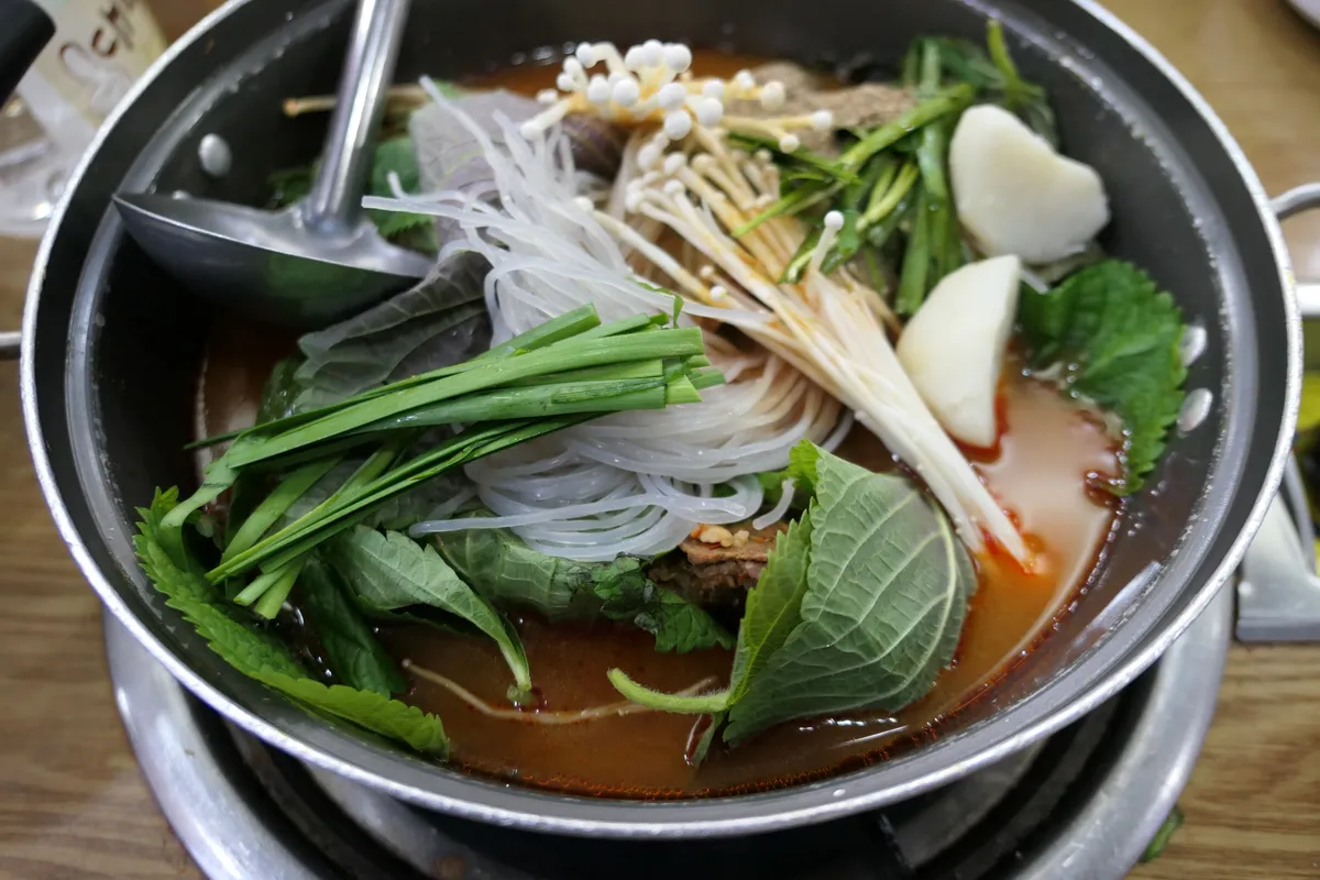 Wide gamjatang pan topped with glass noodles, mushrooms, chives, and leafy greens