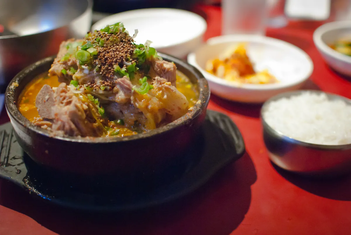 Individual gamjatang pork bone stew served in a black bowl with rice and banchan