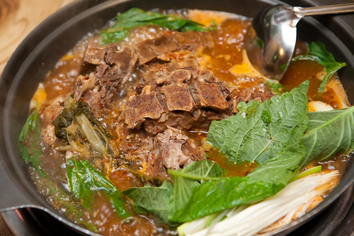 Cooked gamjatang with pork bone pieces, leafy greens, and red broth in a wide pot
