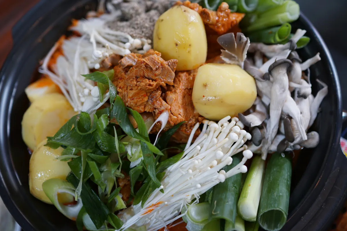 Gamjatang pot arranged with potatoes, pork, mushrooms, green onion, and leafy greens