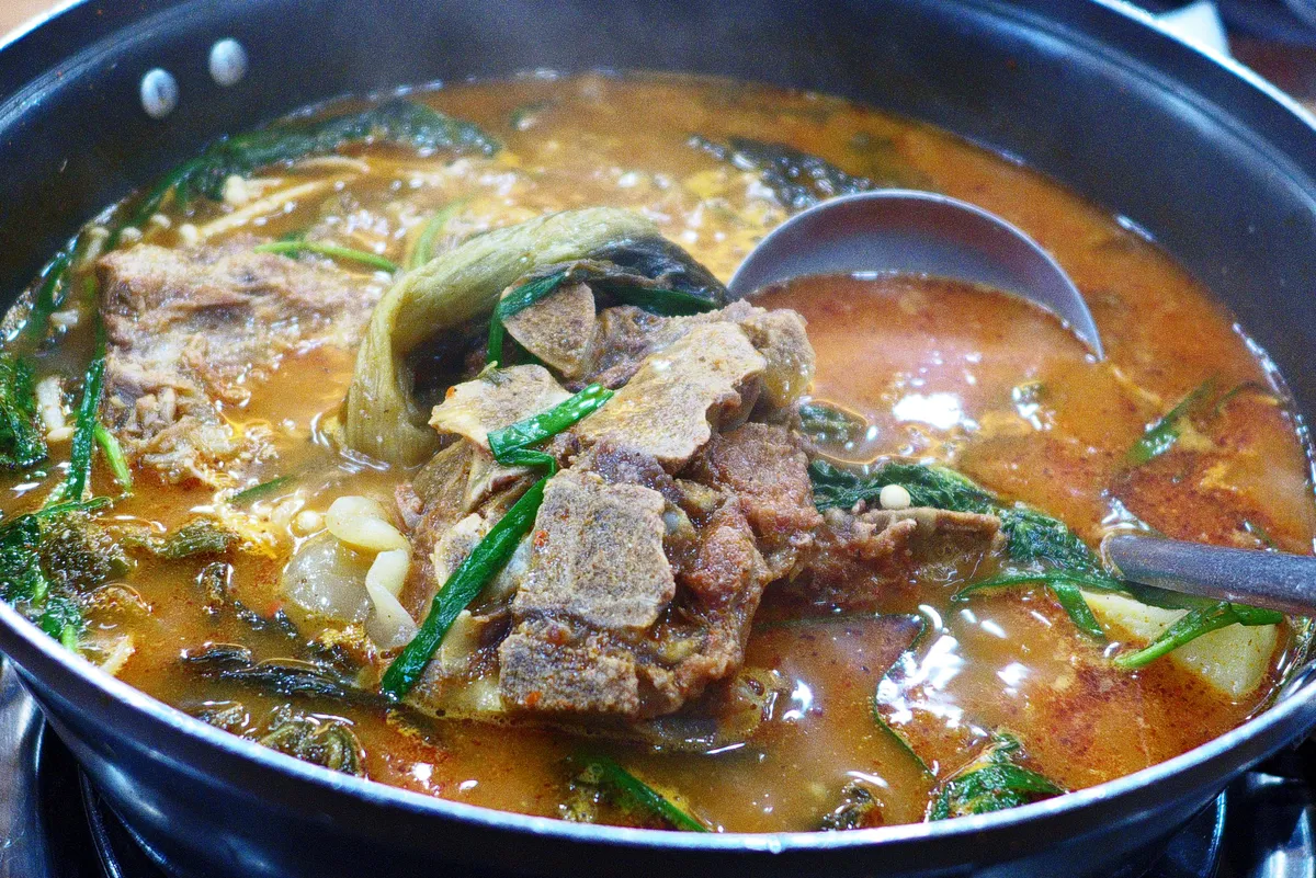 Finished gamjatang with pork bone pieces and greens in red broth
