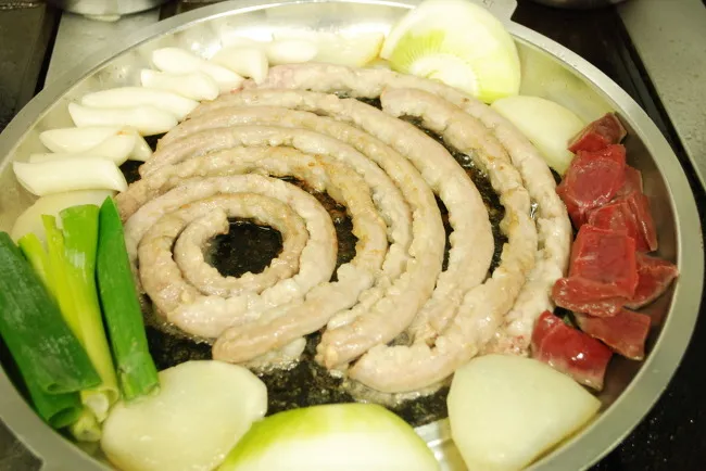 Uncooked gopchang arranged in a spiral with vegetables before grilling