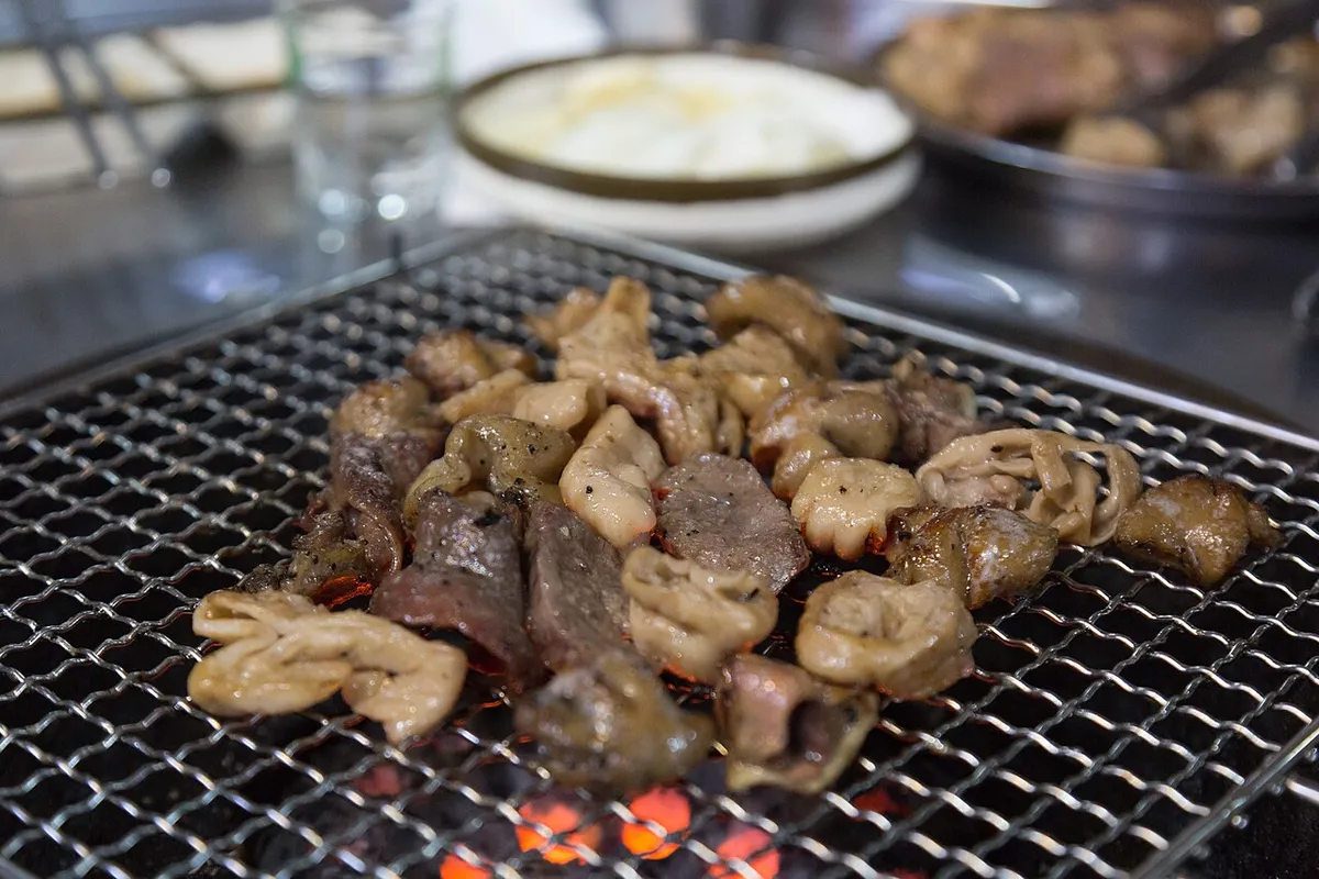 Makchang pieces cooking over a wire charcoal grill