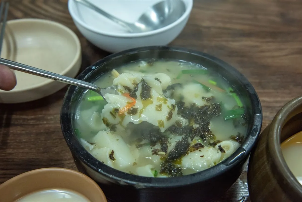 Sujebi hand-torn dough soup topped with seaweed and vegetables in a black bowl