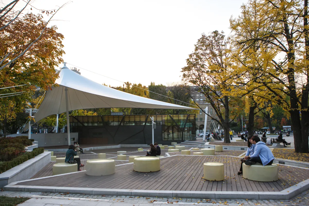 Canopied paved seating area among trees in Marronnier Park in Hyehwa