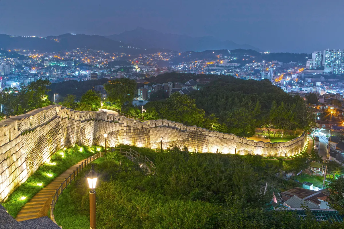 Illuminated Naksan section of the Seoul City Wall above city buildings at night