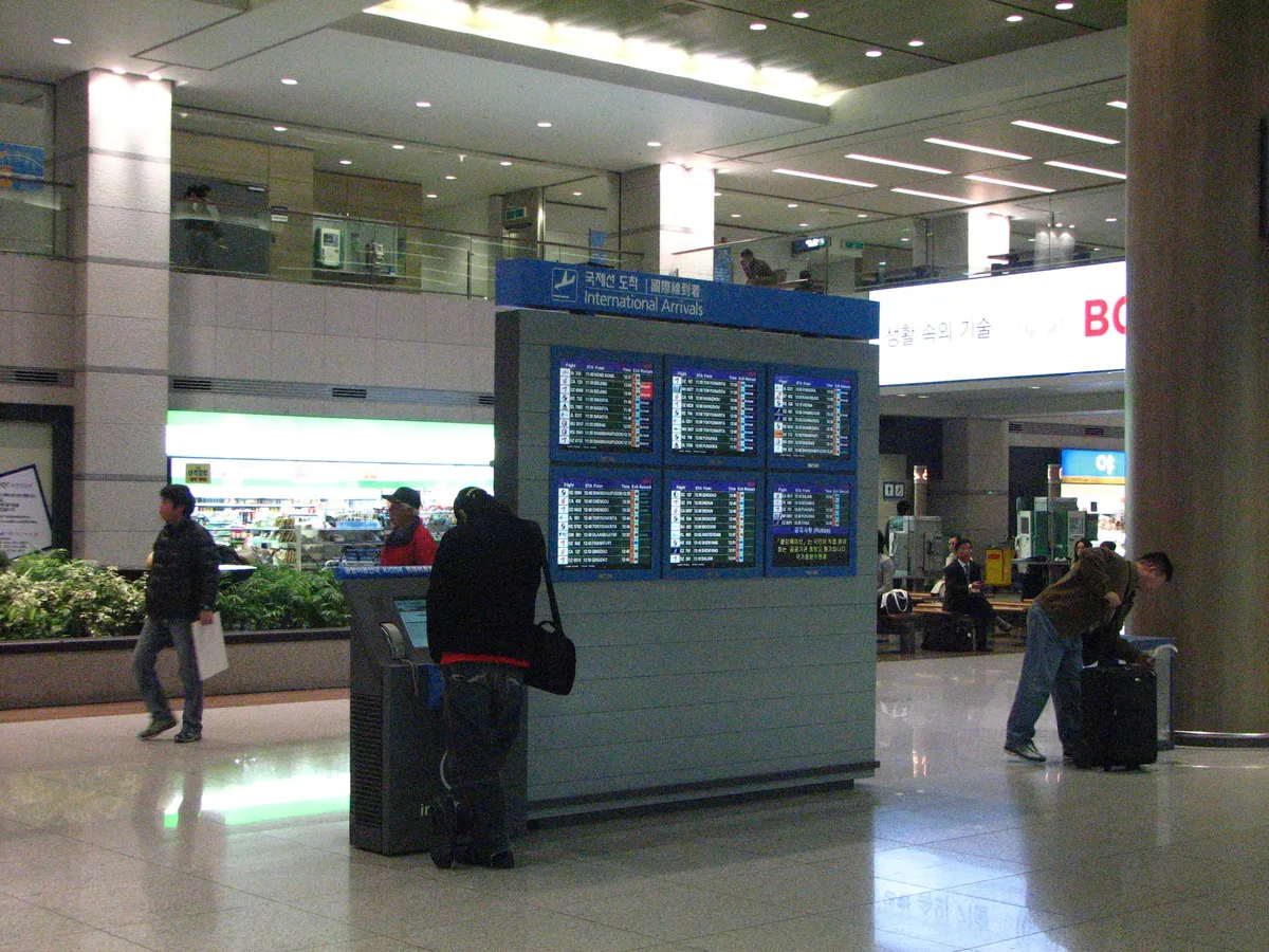 People waiting near an International Arrivals flight-information display at Incheon Airport
