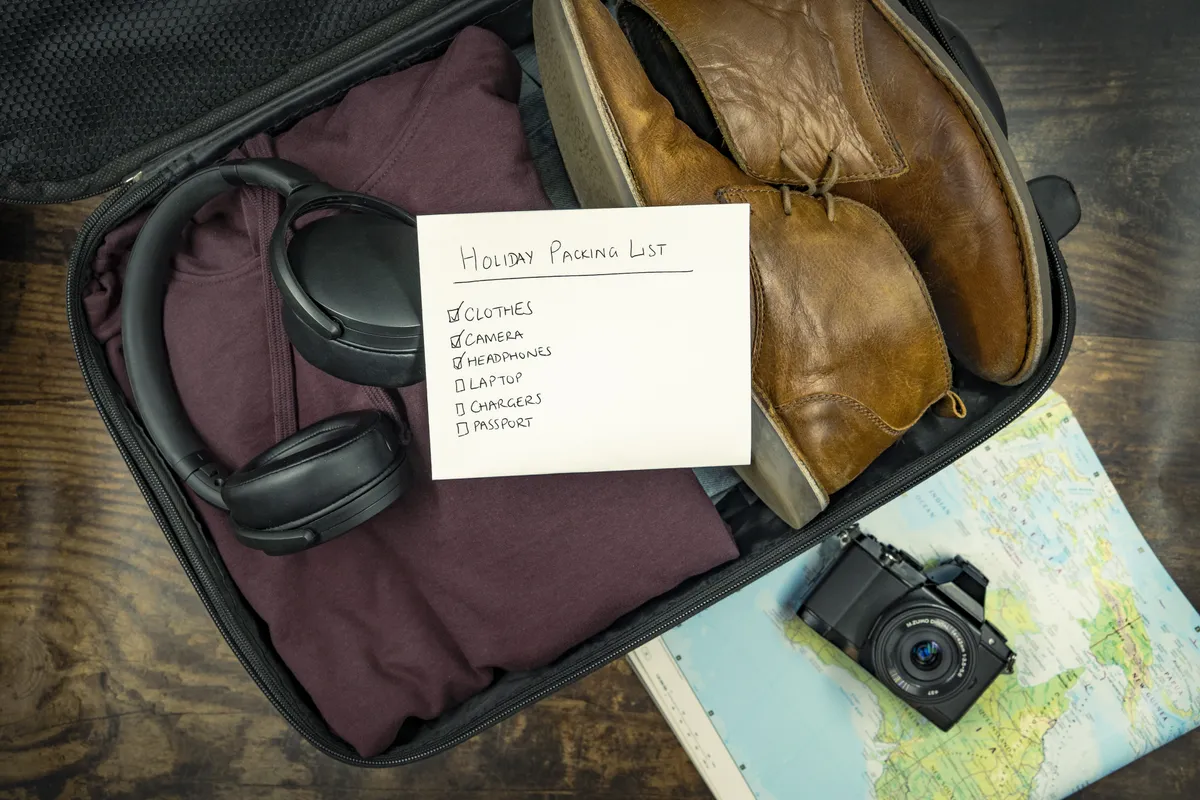 Open suitcase with clothes, shoes, headphones and a handwritten checklist for departure preparation