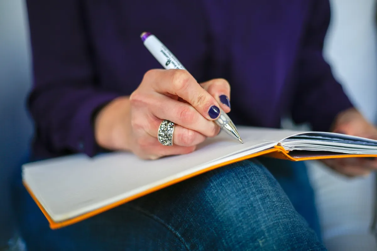 Hand holding a pen above an open notebook for KORAIL Pass travel preparation.