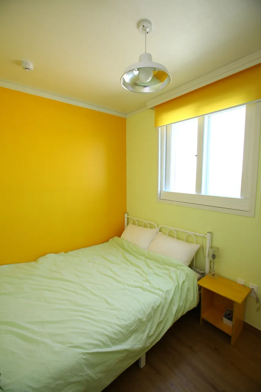 Single raised bed and window in a yellow-walled room at Guesthouse Jip, an illustrative room photograph