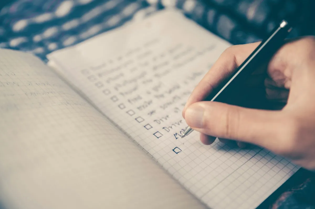 Hand writing a paper checklist to keep essential information alongside Korea travel apps