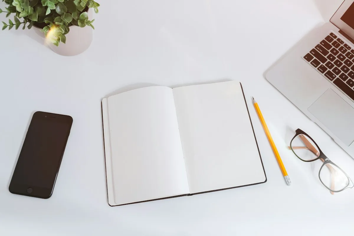Dark-screen smartphone and laptop beside a blank notebook for Korea travel apps preparation