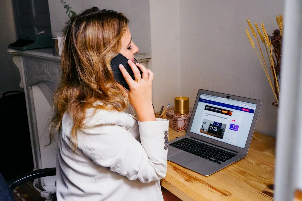 Woman holding a phone to her ear beside a laptop for communication alongside Korea travel apps