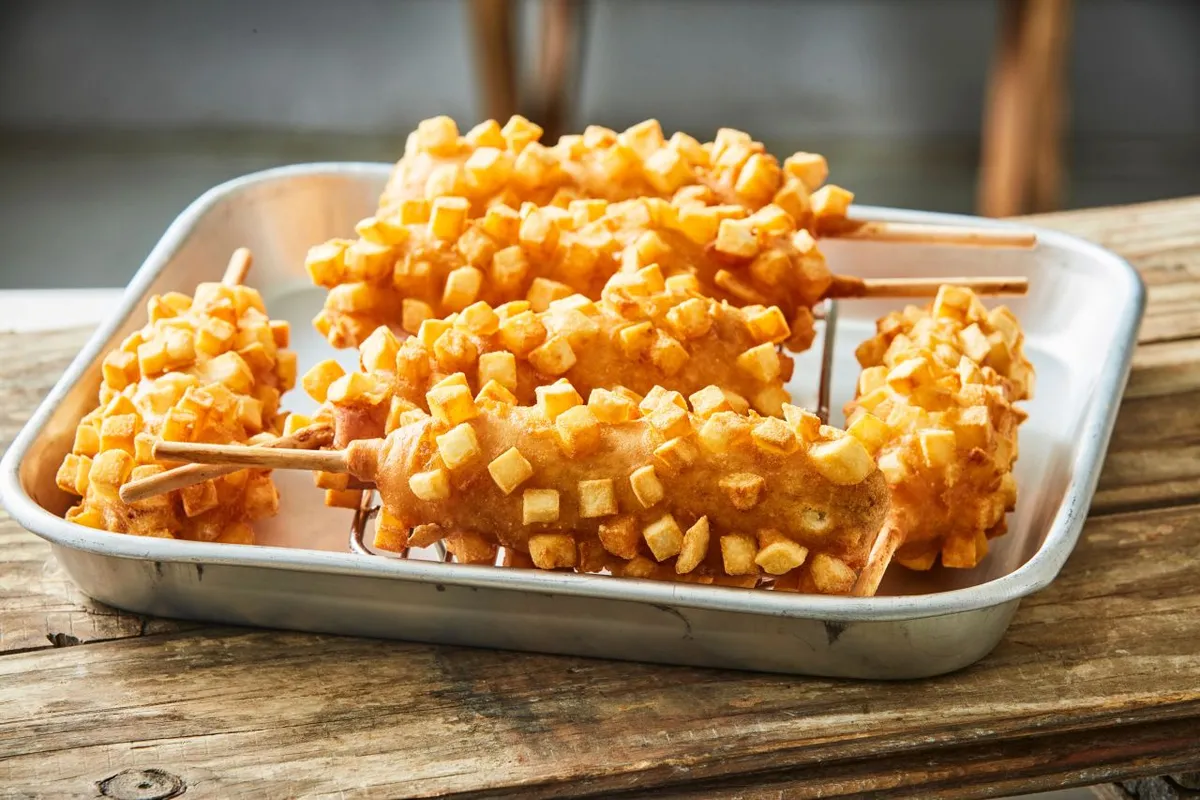 Metal tray piled with potato-coated Korean corn dogs and protruding wooden sticks