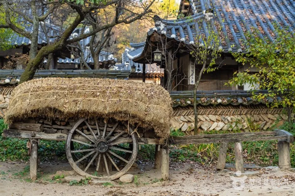 Wooden cart with a straw-covered load beside traditional village buildings