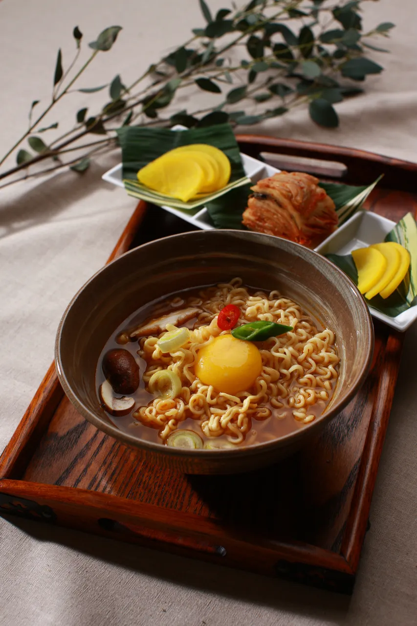 Bowl of Korean ramyeon with egg scallions and kimchi side dishes