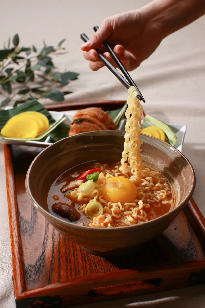 Chopsticks lifting Korean ramyeon noodles from a hot pot