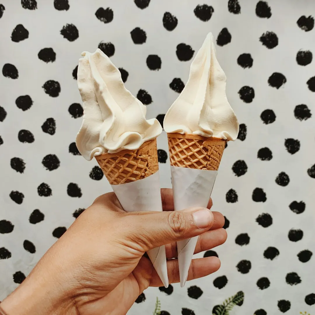 Two vanilla soft-serve cones held in one hand for a Korean yogurt ice cream guide
