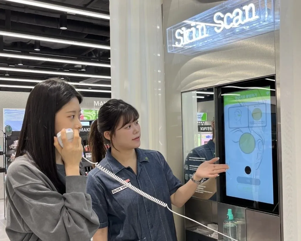 Customer and staff member beside an Olive Young skin-scan touchscreen