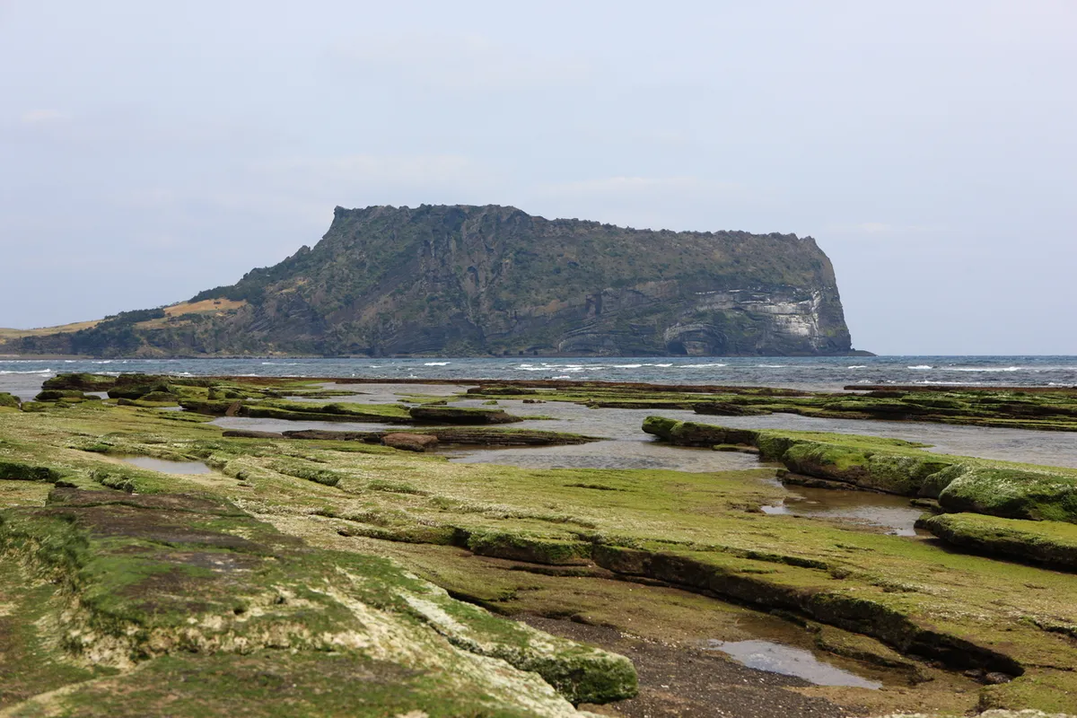 Seongsan Ilchulbong seen across the eastern Jeju shoreline and shallow coastal pools
