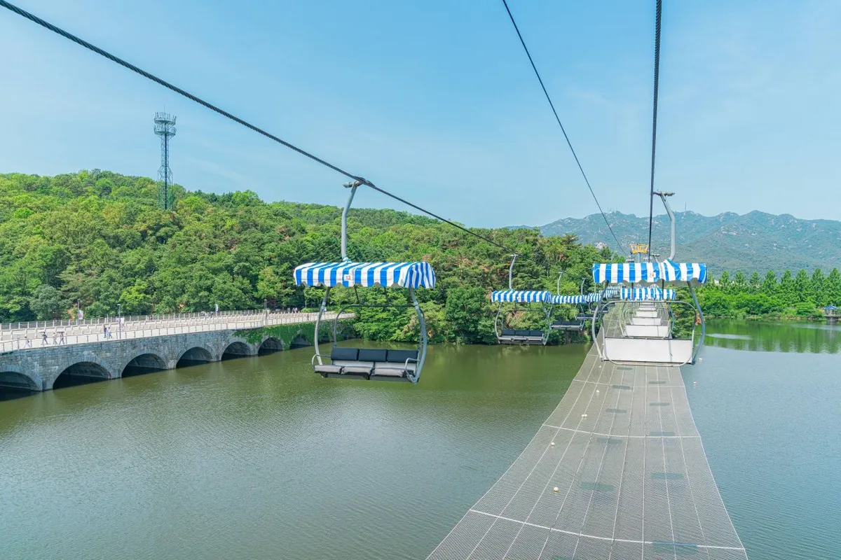 Open Sky Lift chairs with striped canopies crossing the lake at Seoul Grand Park