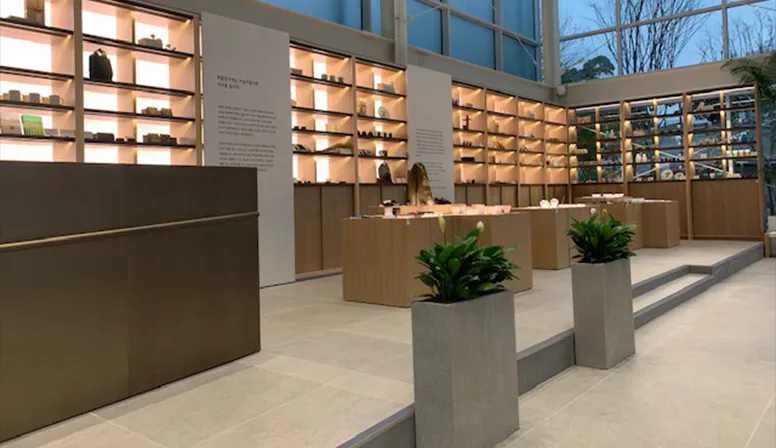 Seoul Museum of Craft Art shop with illuminated shelves, pale wood counters and shallow steps beside tall planters