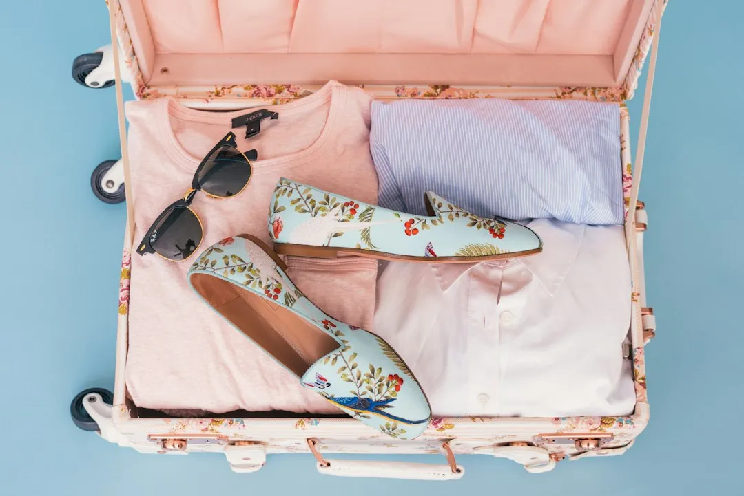 Open pink-lined suitcase with folded clothes, shoes and sunglasses for final pre-departure budget checks