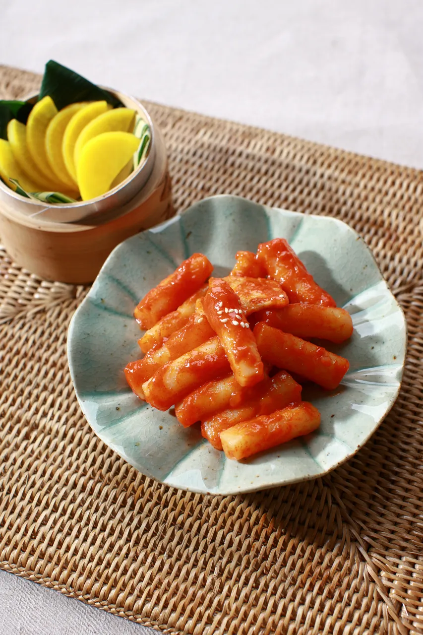 Red tteokbokki rice cakes served on a plate with fruit garnish