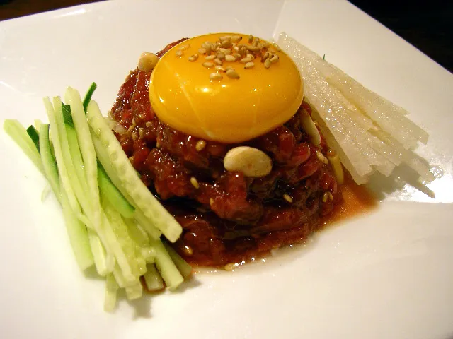 Yukhoe with egg yolk, cucumber strips, pear, and garlic
