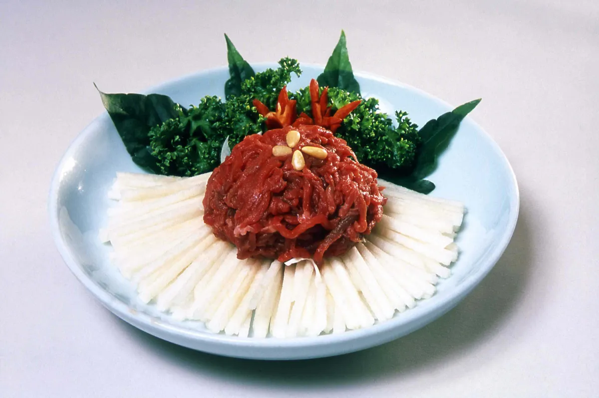 Korean yukhoe served with pear slices and leafy greens